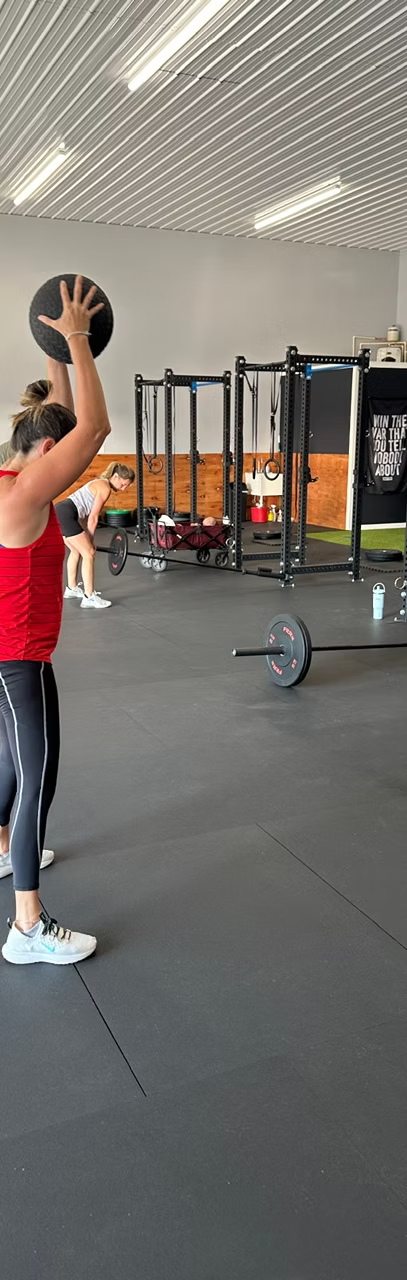 A member lifts a medicine ball overhead during class